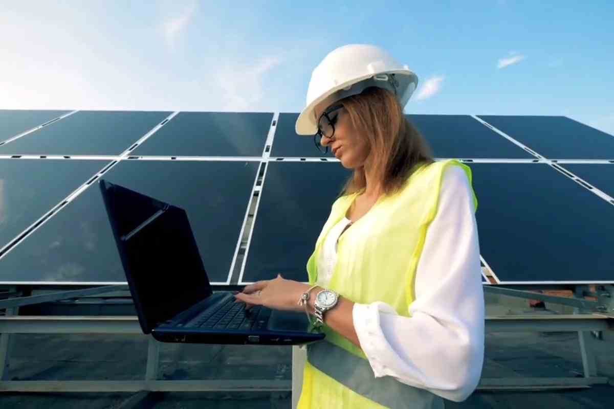 donna su un cantiere con fotovoltaico e tra le mani un portatile