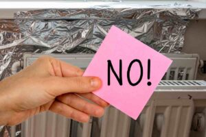 carta stagnola dietro i termosifoni e una mano che tiene un post-it con la scritta no